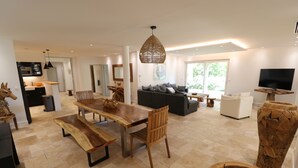 Ein modernes Wohnzimmer mit einem Holzesstisch, einer Couch und einem an einem Baumstamm montierten Fernseher.