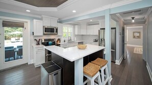 Une cuisine moderne avec des meubles blancs, un îlot central et une vue sur l’extérieur.