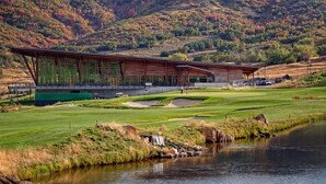 En modern byggnad med en stor glasfasad, belägen på en golfbana med en vattendekoration i förgrunden.