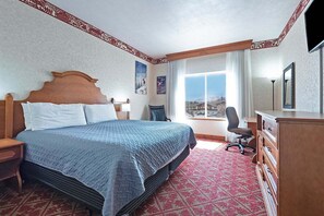 Ein Hotelzimmer mit einem großen Bett, einem Schreibtisch, einem Stuhl, einem Schminktisch und einem Fenster mit Blick auf einen Berg.