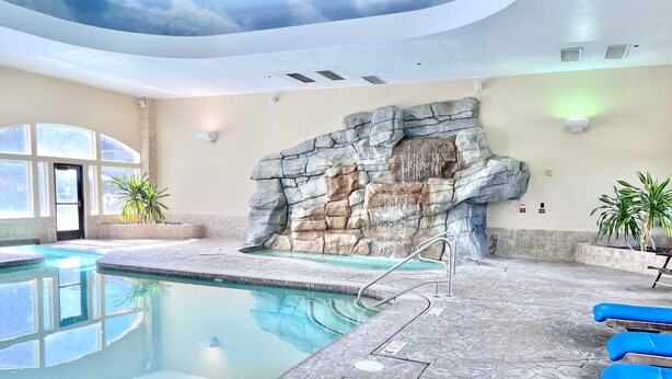 An indoor swimming pool with a rock wall, clear ceiling, and blue lounge chairs. - 231 | Premium Escape | 2Q Near Sundance + Park City (Midway)
