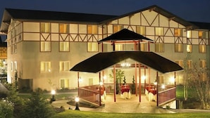 Un edificio grande de varios pisos con un estilo arquitectónico europeo tradicional, que cuenta con una entrada destacada con una galería cubierta y un área de estar al aire libre.