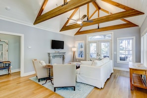 Cozy living area with a fireplace, armchairs, and a sofa, featuring a flat-screen TV and large windows.