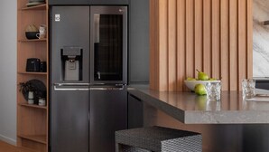 Cocina moderna con refrigerador negro integrado, panel de pared de madera y una pequeña isla con un cuenco de fruta y vasos.