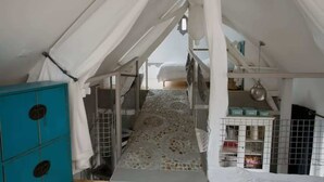 Una habitación con tienda de campaña, suelo estampado, un mueble de color turquesa y una cama con dosel blanco.