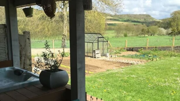 Un patio con mesa y sillas, un jacuzzi y vistas a un campo verde y colinas.