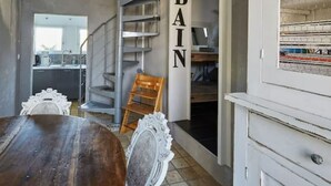 Un comedor con una mesa de madera y sillas decoradas, una escalera y una cocina visible al fondo.