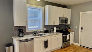 A modern kitchen with white cabinets, a stainless steel dishwasher, a microwave, and a stove.