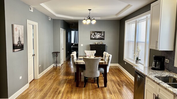 A dining area with a wooden floor, a chandelier, and a dining table with chairs.