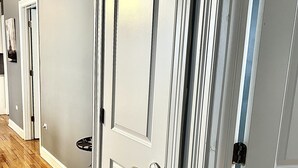 A hallway with wooden flooring, white doors with silver handles, and a light gray wall.
