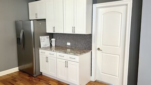 A compact kitchen with white cabinets, a stainless steel refrigerator, and a tiled backsplash.