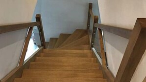 Eine Holztreppe mit Glastrennläufern, die zu einer Empfangsebene mit einer Leuchte führt.