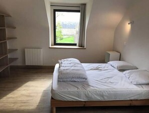 Un dormitorio con cama, ventana, radiador y mesita de noche.