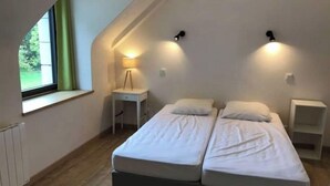 Ein kleines, modernes Schlafzimmer mit zwei Einzelbetten, einem Schreibtisch und einer Lampe.