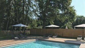Ein rechteckiger Swimmingpool mit klarem, blauem Wasser, umgeben von einer Holzterrasse. Liegestühle und Sonnenschirme bieten Schatten.