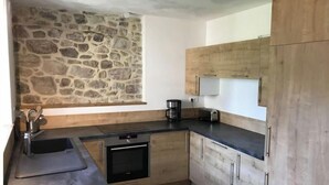 Eine moderne Küche mit Steinwand, Holzschränken, integriertem Backofen und einer Kaffeemaschine.