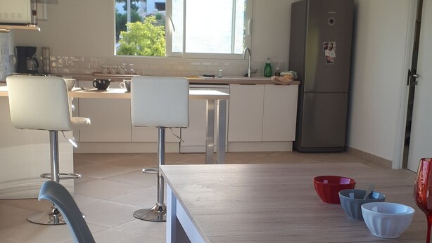 A modern kitchen with a dining area, featuring a long wooden table, two bar stools, and a refrigerator. - PRETTY VILLA, independent, close to the beach, the mountains, the shops! (VENTISERI)