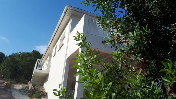 A white building with a balcony, surrounded by greenery.