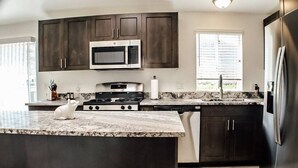 A modern kitchen with dark cabinets, a stainless steel microwave, a gas stove, and a built-in dishwasher. - "Trail Leader" Newly Remodeled Single Family Home (Moab)