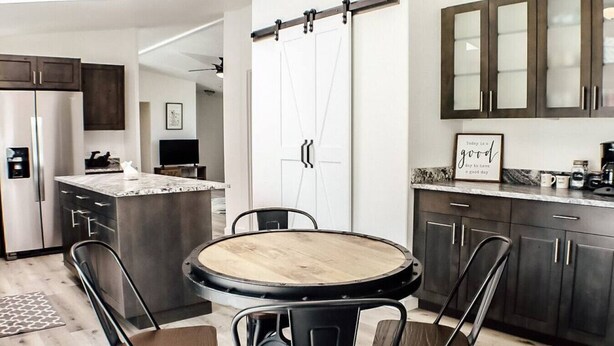 A modern kitchen with dark cabinets, a central island, and a round table with chairs. - "Trail Leader" Newly Remodeled Single Family Home (Moab)