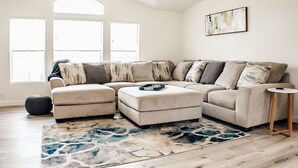 A modern living room with a sectional sofa, a round ottoman, and a small side table. - "Trail Leader" Newly Remodeled Single Family Home (Moab)