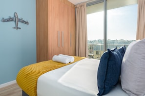 Ein Hotelzimmer mit Bett, einem Holzschrank, einem Fenster mit Blick auf die Stadt und einem Handtuch auf dem Bett.