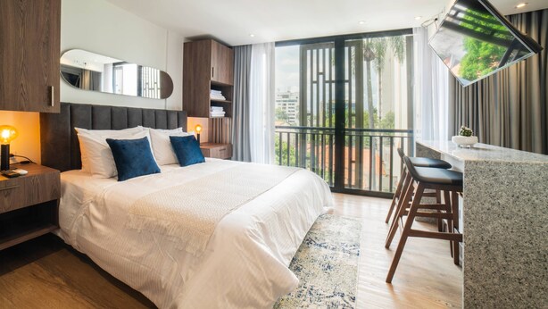 A modern bedroom with a large bed, a desk, and a balcony with a view.