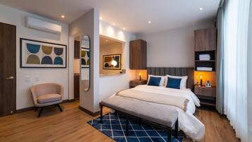 Quarto de hotel moderno com uma cama grande, uma mesa de cabeceira com abajur, uma cadeira e um guarda-roupa.