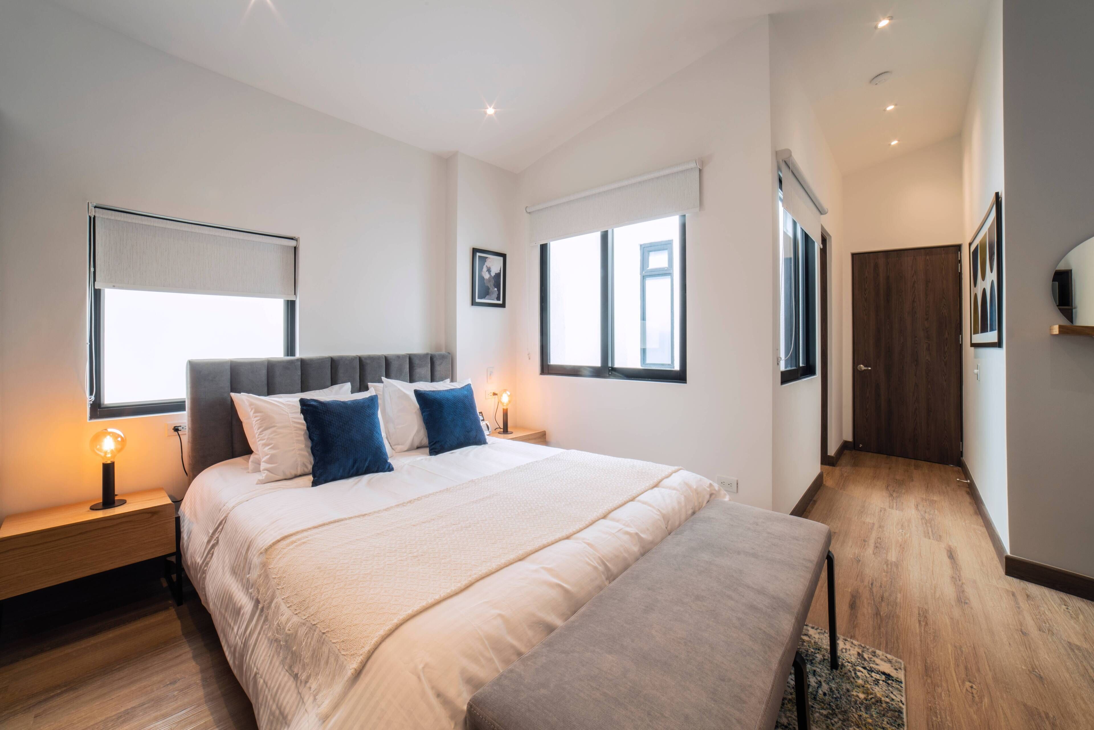 Una camera da letto moderna con un letto grande, abat-jour, pavimento in legno e vista sul corridoio.