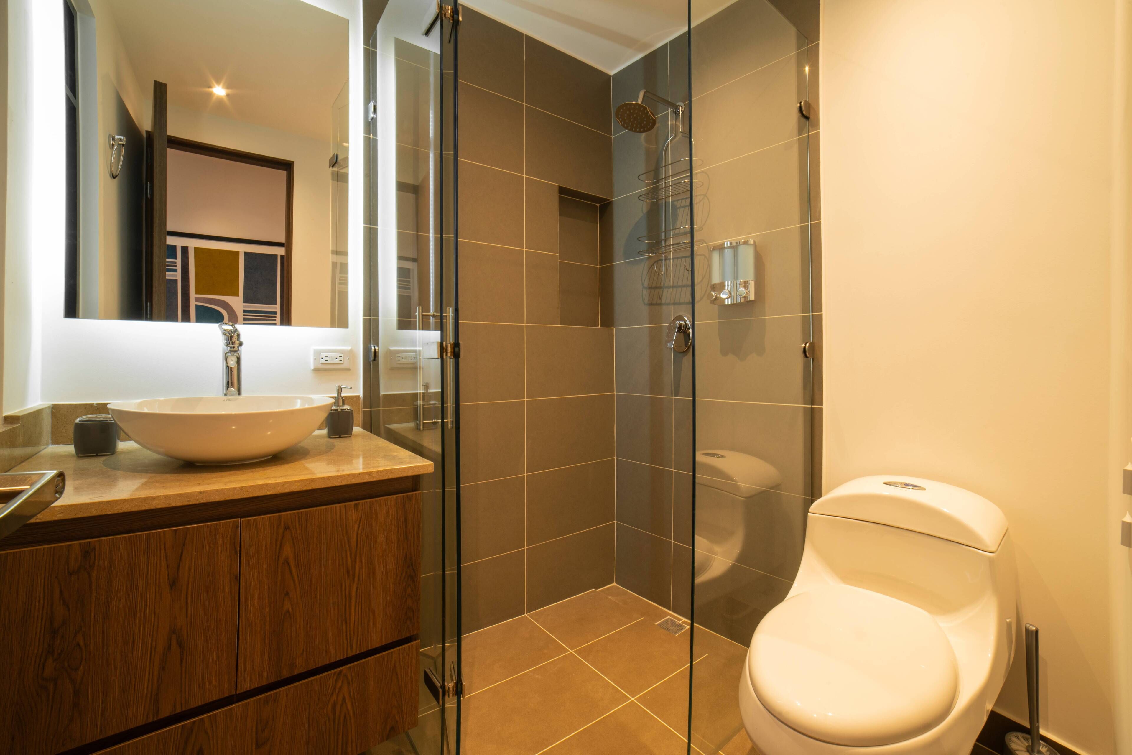 A modern bathroom with a glass-enclosed shower, a wooden vanity, and a white toilet.
