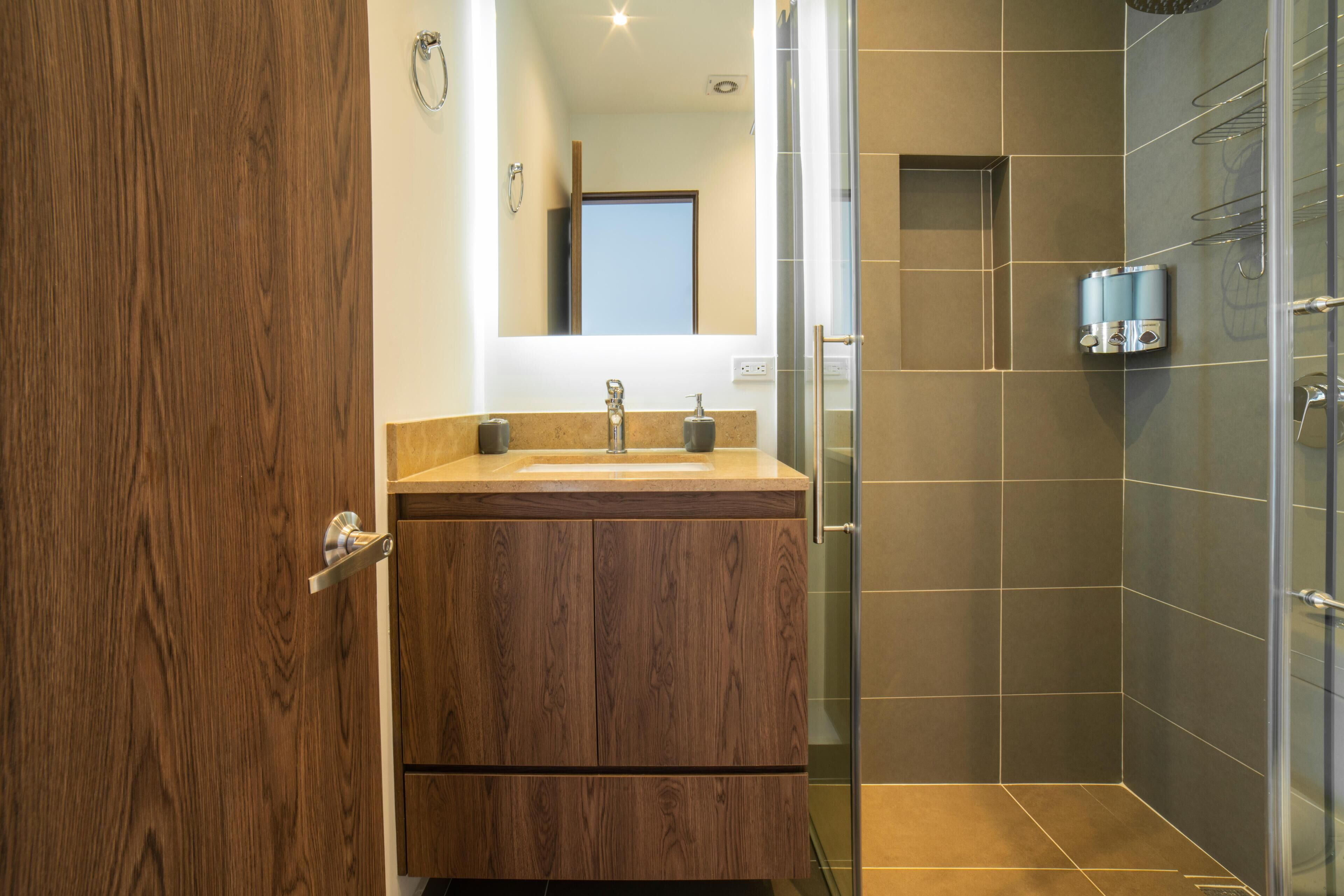 Un baño moderno con tocador de madera, cabina de ducha de vidrio y espejo sobre el lavabo.