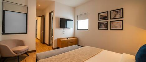 A hotel room with a bed, a chair, a dresser, a television, and framed pictures on the wall.