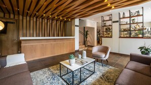 A modern living room with a wooden ceiling, a central coffee table, a sofa, and a decorative shelf with plants.