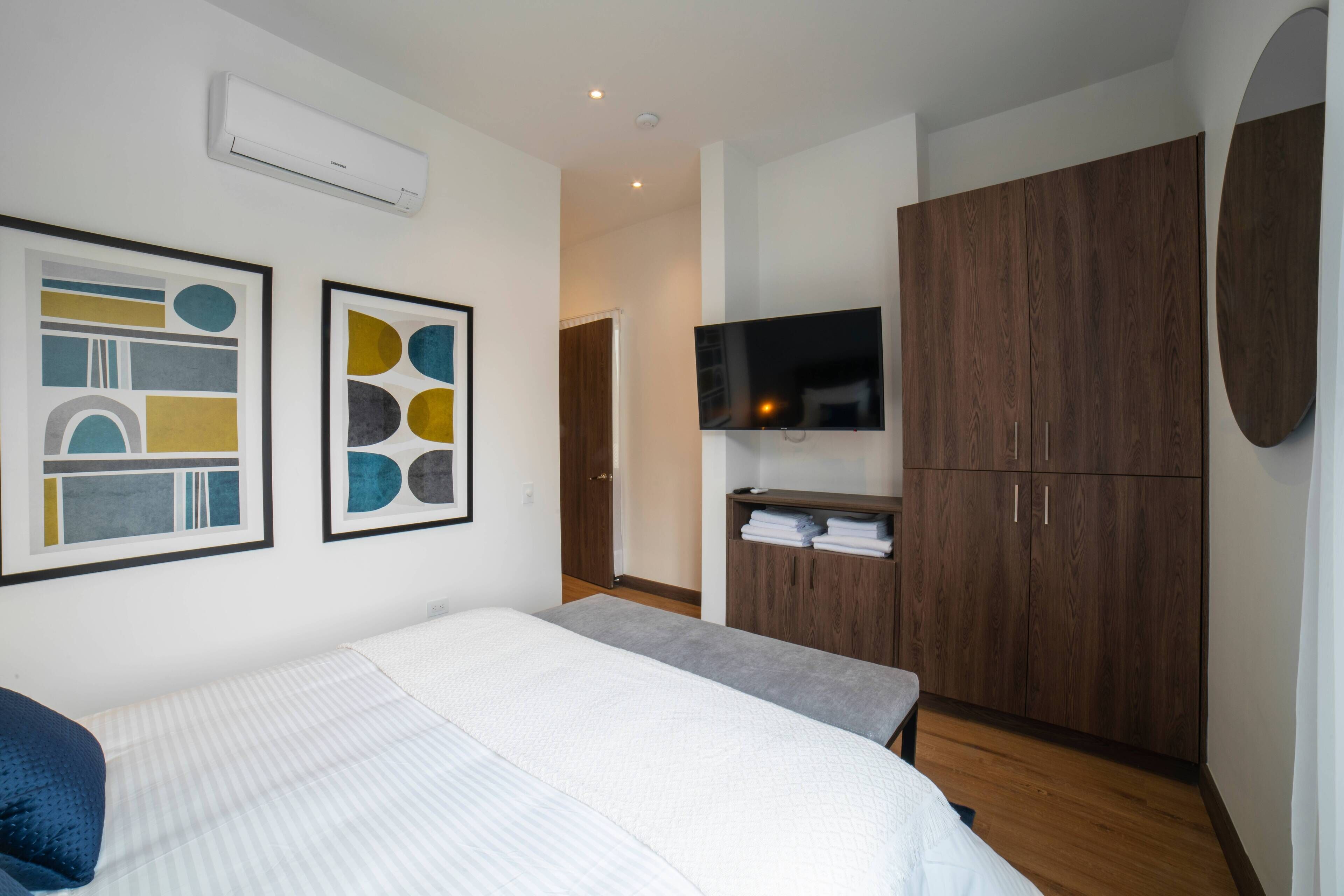 A modern bedroom with a large bed, a wardrobe, a flat-screen TV, and abstract art on the wall.