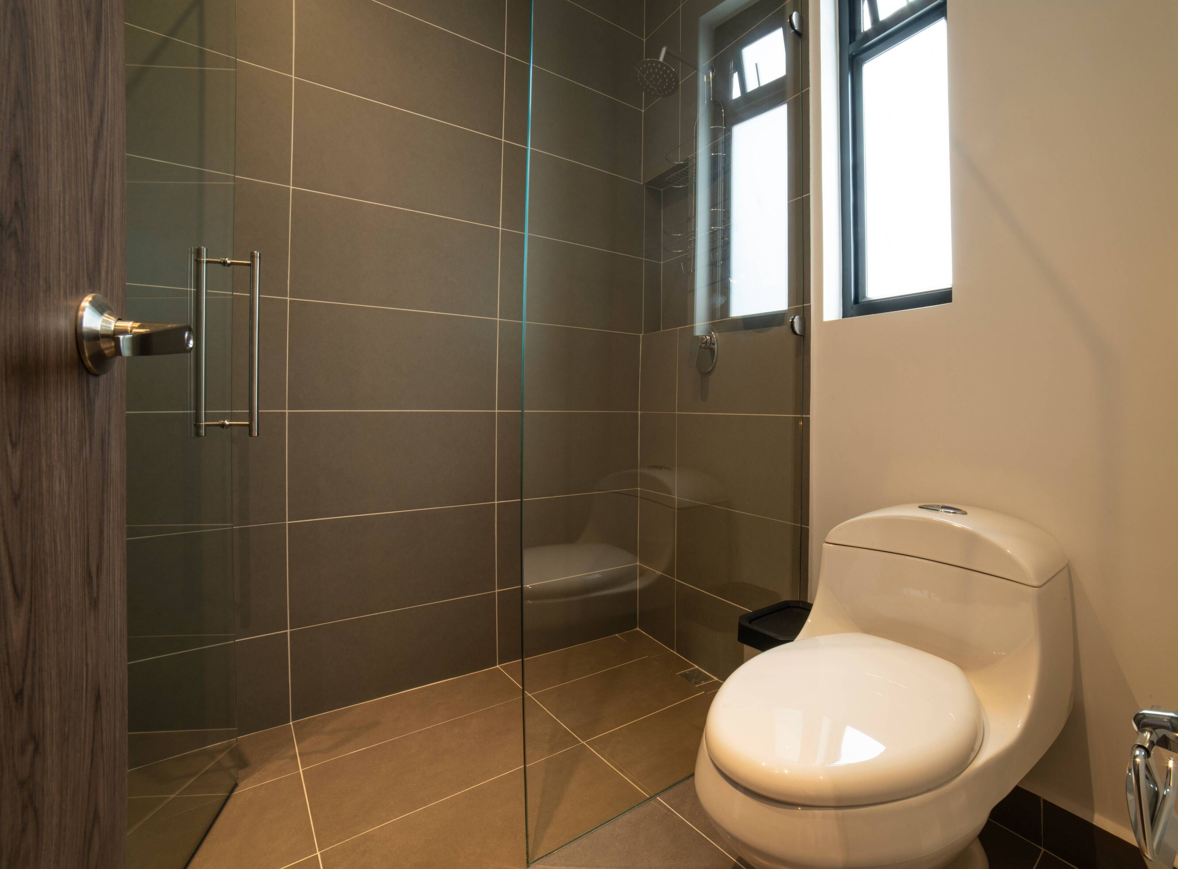 Ein modernes Badezimmer mit Duschkabine aus Glas, Toilette und einem Fenster für natürliches Licht.