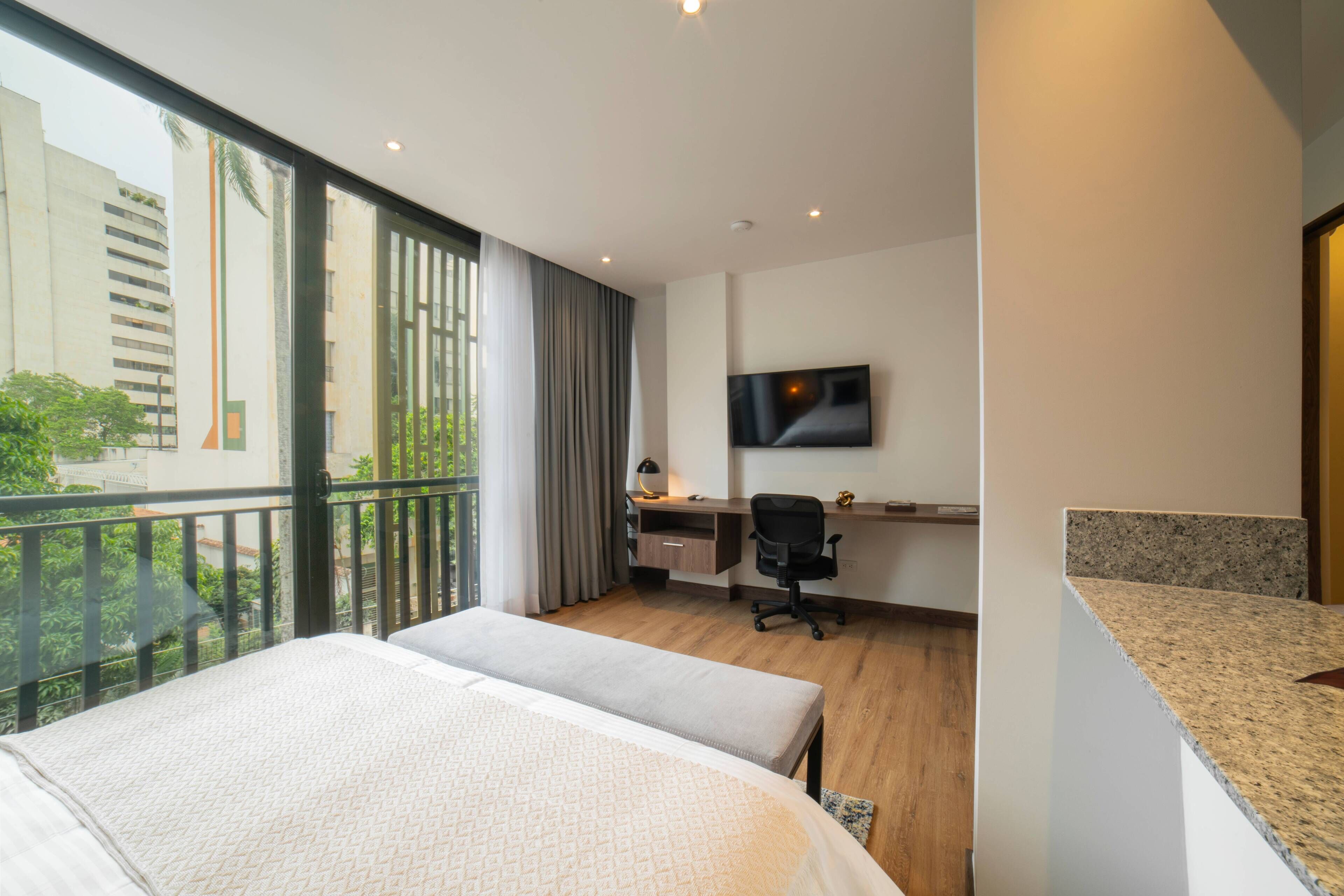 Una habitación de hotel con un ventanal grande, un escritorio, una silla, una cama y un televisor en la pared.