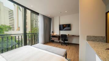 Una habitación de hotel con un ventanal grande, un escritorio, una silla, una cama y un televisor en la pared.