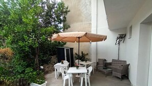 A patio with white tables and chairs, a beige umbrella, and a wicker sofa. - La Fenice Budoni (Budoni)