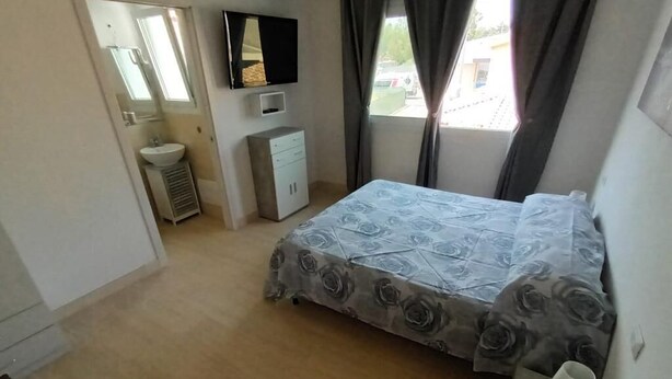 A bedroom with a bed, a TV, a wardrobe, a sink, and a window with curtains. - La Fenice Budoni (Budoni)