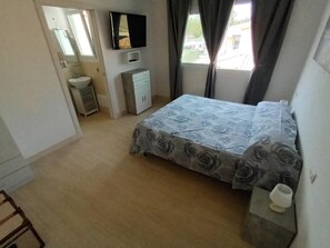 A bedroom with a bed, a TV, a wardrobe, a sink, and a window with curtains. - La Fenice in Budoni (Budoni)