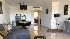 Uma sala de estar moderna com um sofá cinza, uma mesa de centro redonda e um espaço de jantar com mesa e cadeiras de madeira.
