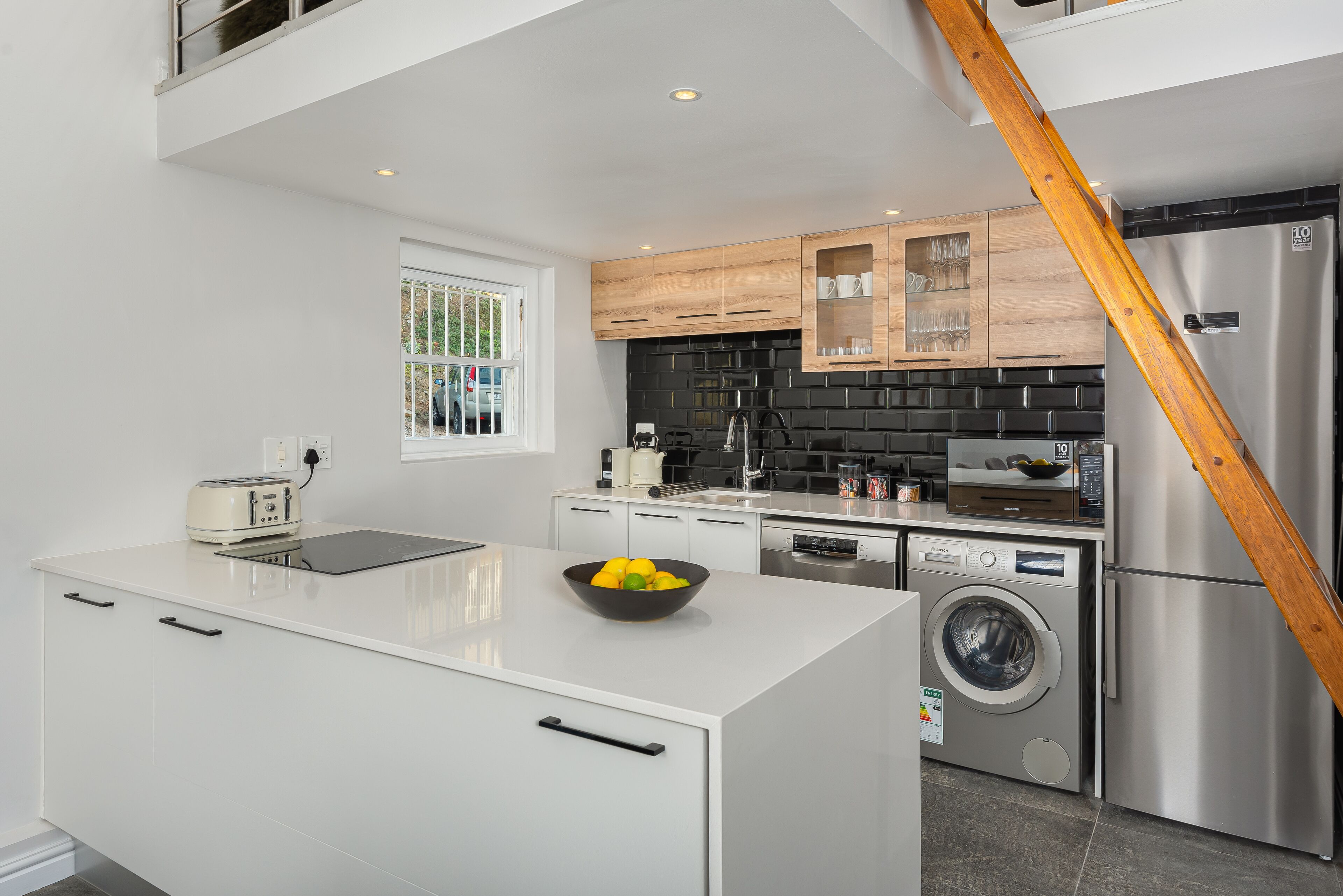 A modern kitchen with white cabinetry, a built-in washing machine, and a wooden staircase.