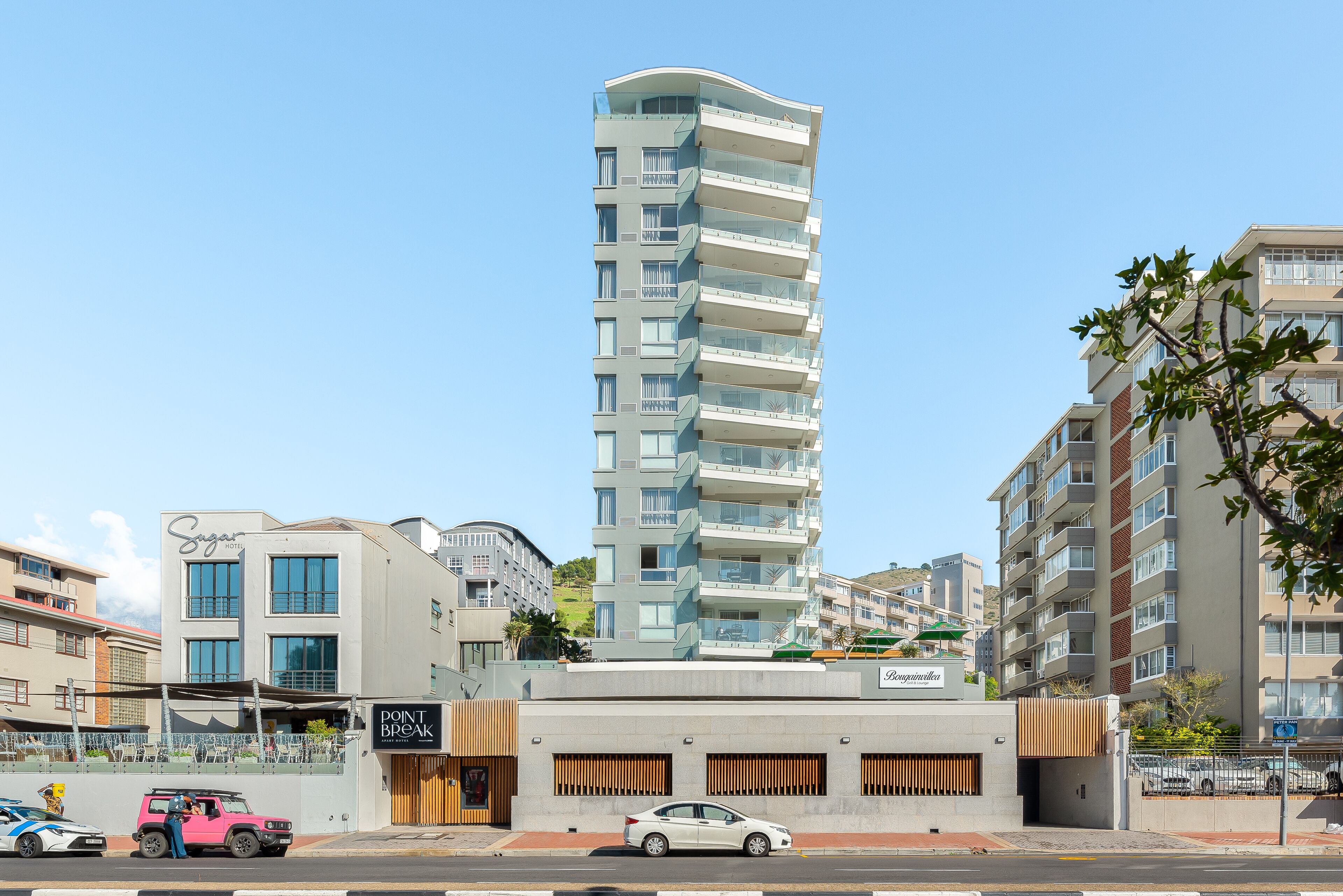 A modern high-rise hotel with multiple balconies, a ground-level restaurant, and a parking area.