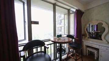 Una habitación con balcón, una mesa de comedor con sillas, un espejo y un pequeño escritorio.