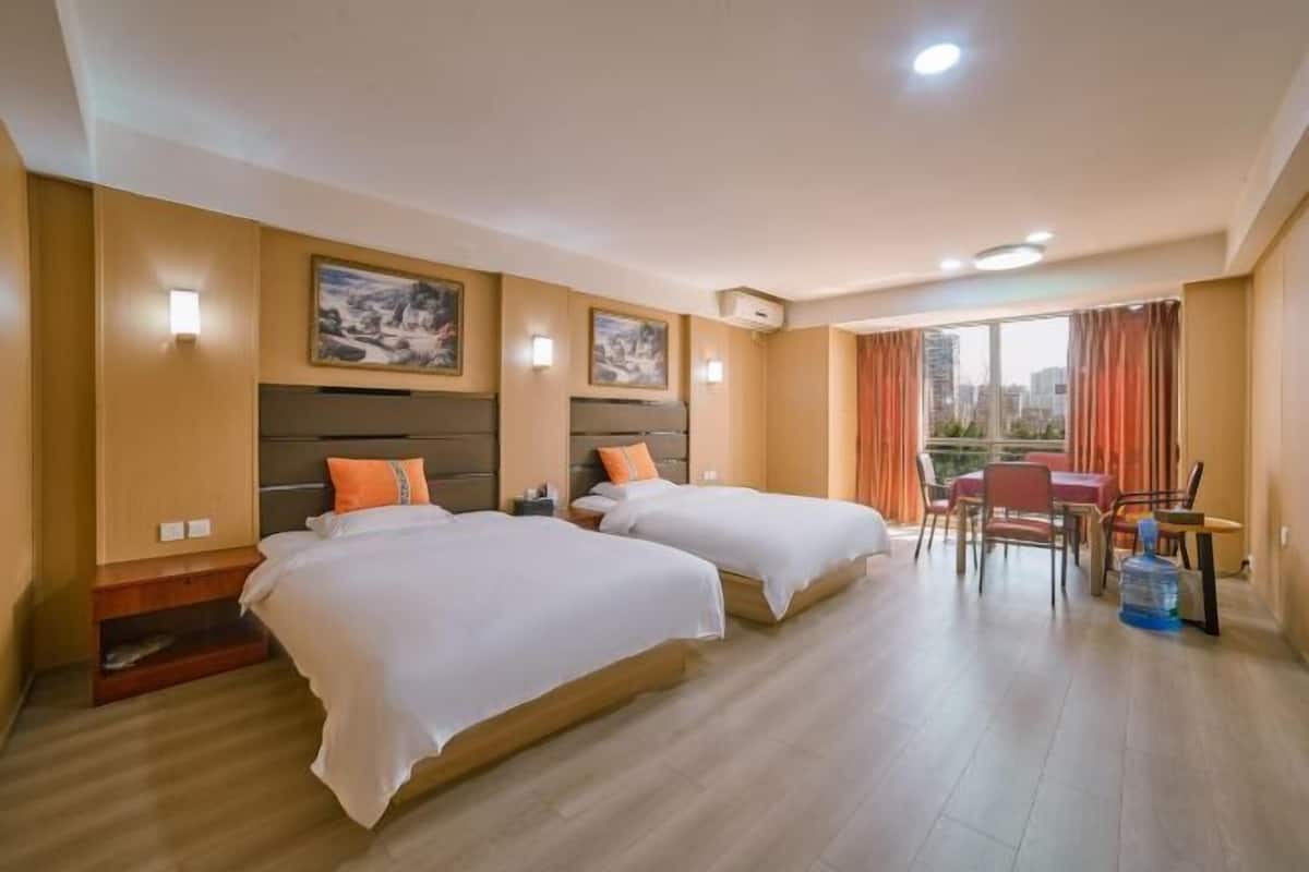 Habitación de hotel con dos camas, una mesa de comedor y vistas a la ciudad.