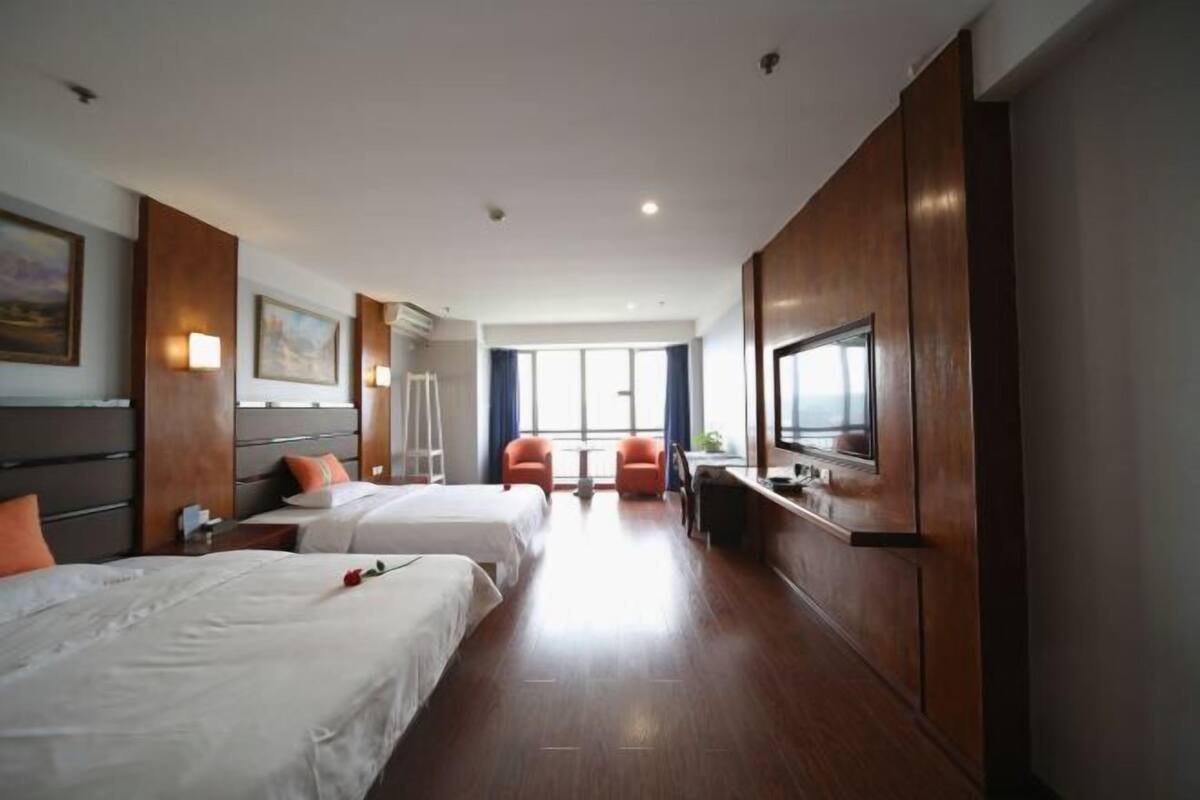 Una habitación de hotel con dos camas, un escritorio, un televisor y un ventanal grande.