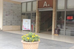 Une entrée d’immeuble avec un escalier, un pot de fleurs et des panneaux d’information.