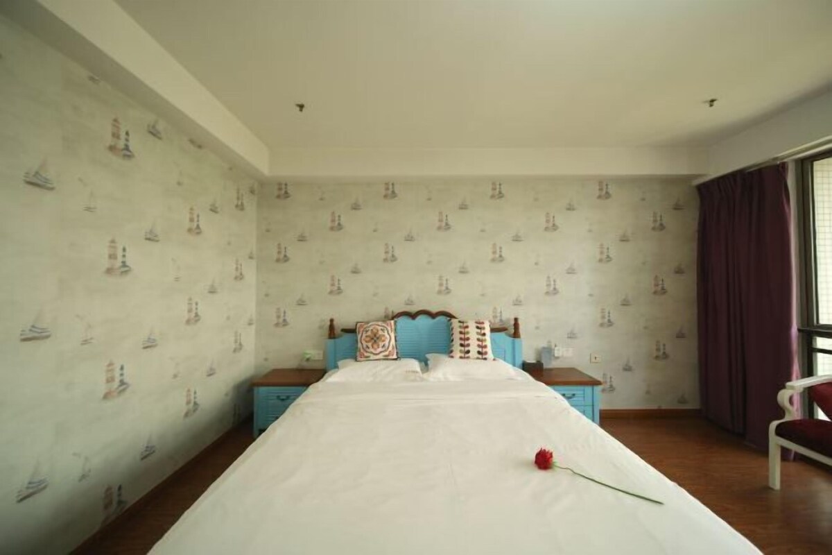 Quarto com cama, mesa de cabeceira, cadeira e janela com cortinas.