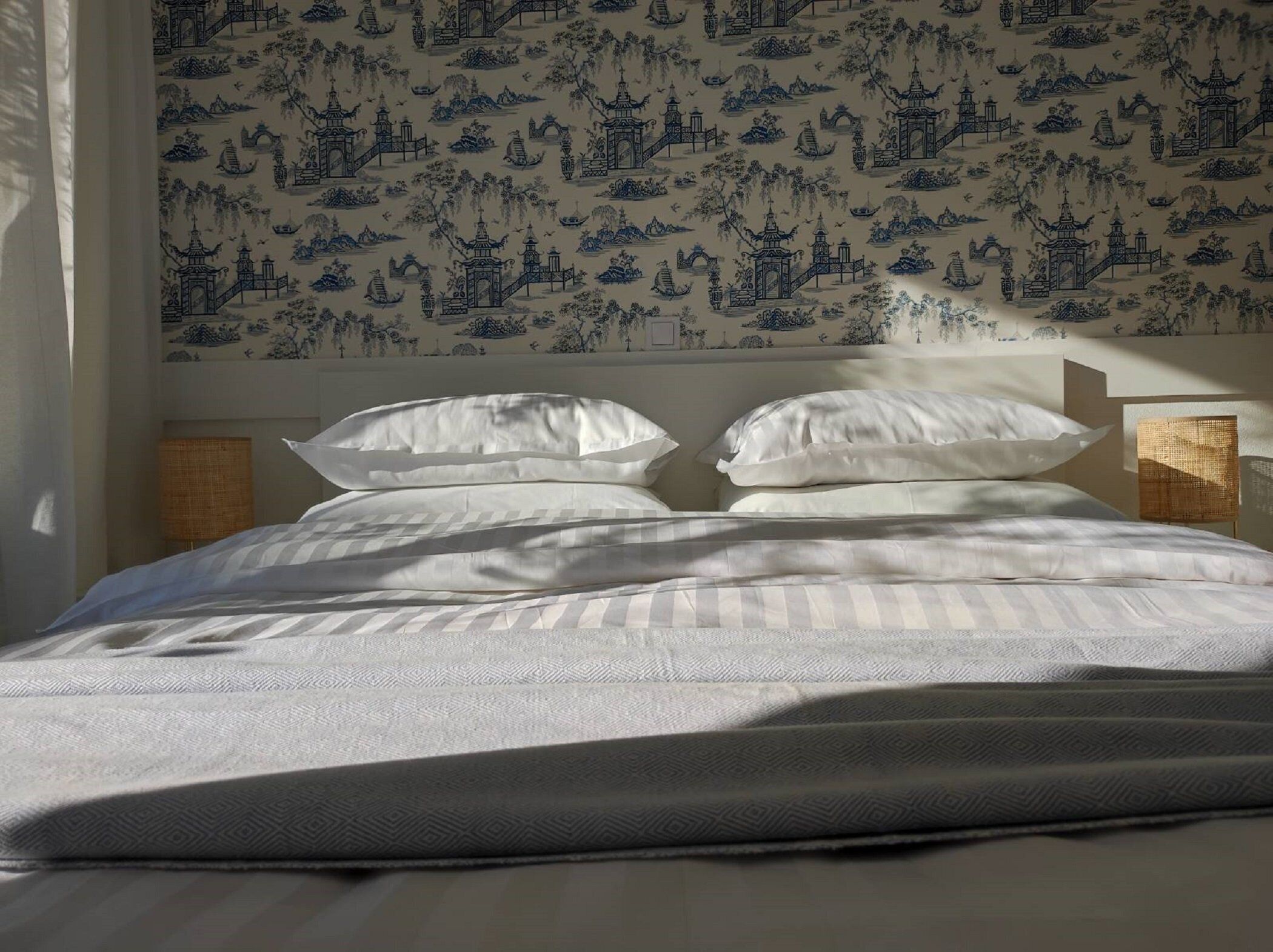 Ein Bett mit weißer Bettwäsche und einer gemusterten Wand dahinter.