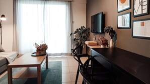 Ett modernt vardagsrum med en soffa, ett soffbord och en matplats med stolar. Det finns en tv monterad på väggen och ett fönster med gardiner.